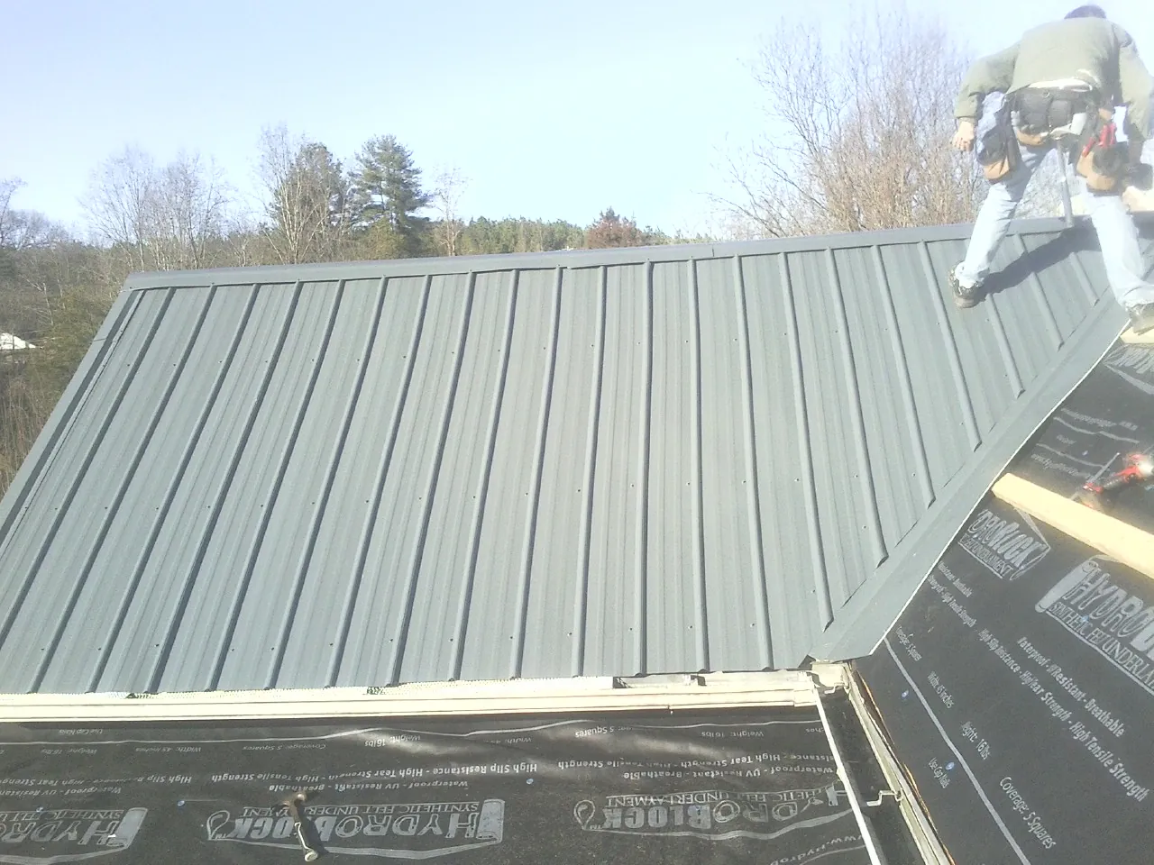 Crew installing dark green standing seam panels over synthetic underlayment in New Castle