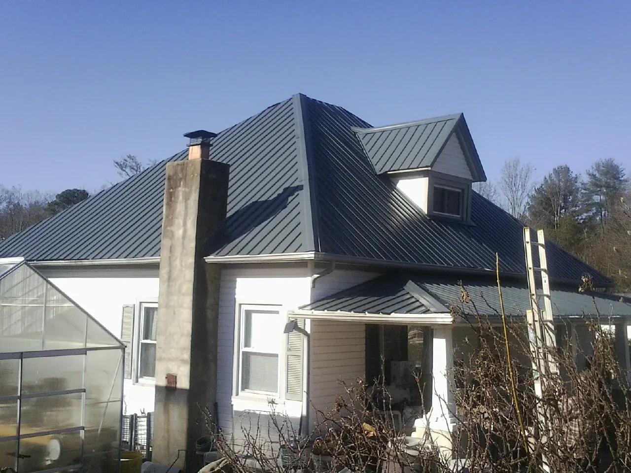 Dark blue standing seam metal roof on a white farmhouse with dormer — Slate & Tile Roof Repair by Roofing Brothers in New Castle
